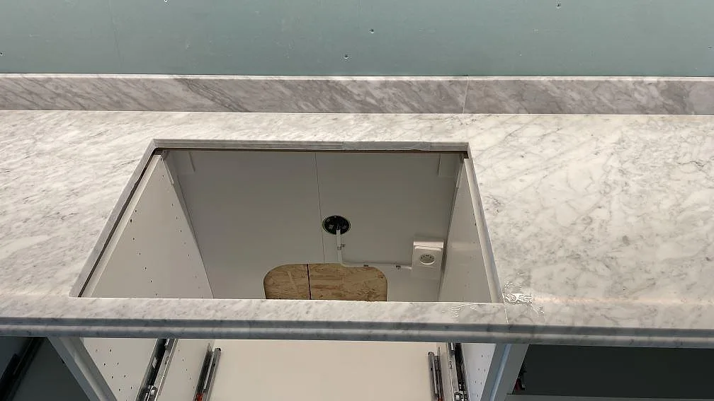 Matt Carrara C marmorbänkskiva med rektangulär öppning för häll och uppvikt stänkkant i ett kök i Malmö.