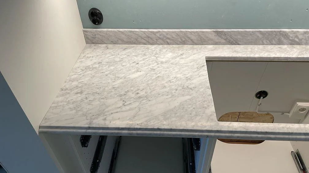 Hörnvy av matt Carrara C marmor med hällöppning, ljus ådring och låg stänkkant i ett kök i Malmö.