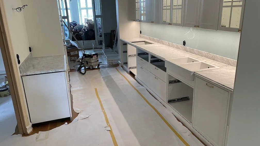 Matt köksbänkskiva i Carrara C marmor med uppvikt stänkkant, vit dubbelho och sidobänk under montering i Malmö.