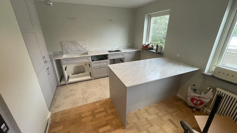 Matt köksbänkskiva och köksö i Carrara C marmor i ett kök under montering i Malmö.
