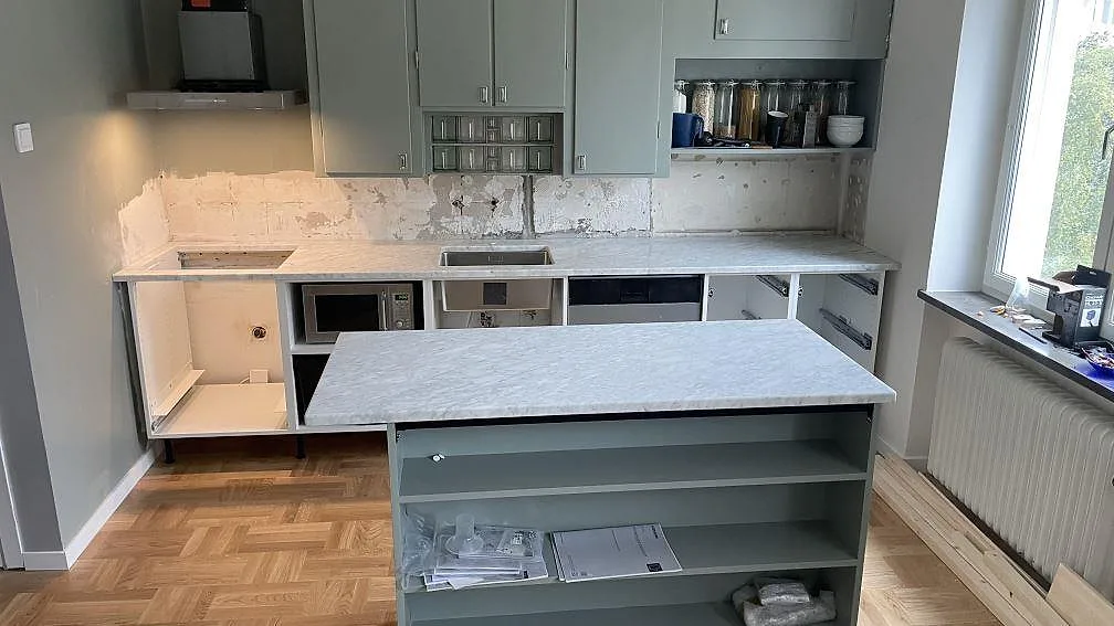 Köksbänkskiva och köksö i matt Carrara C-marmor i ett kök under montering i Malmö.