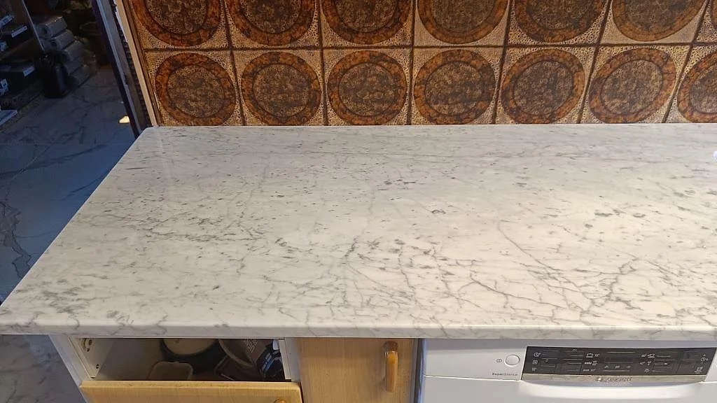 Närbild av polerad Carrara C som köksbänkskiva med grå ådring över en rak arbetsyta i Mellbystrand.