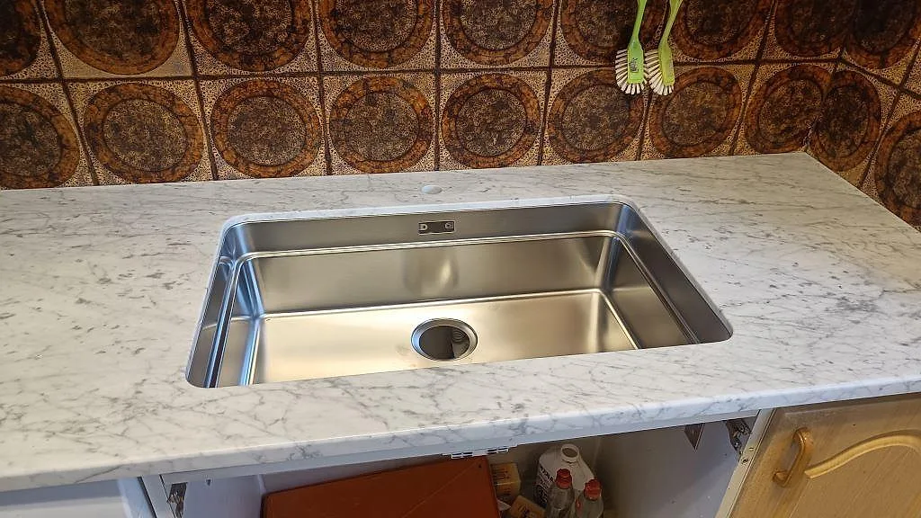 Diskhozon i kök med polerad Carrara C, 30 mm marmor, där den rostfria diskhon syns mot den gråvita ådringen i Mellbystrand.