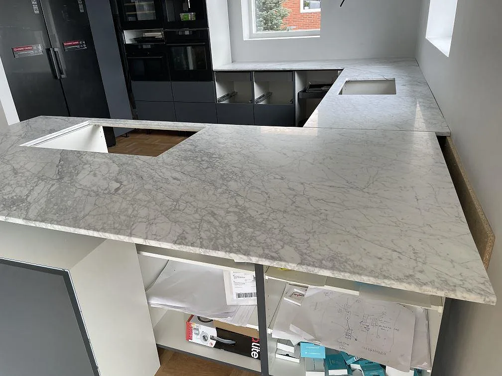 Installerad köksbänkskiva i matt Carrara C marmor med mörka köksstommar och öppningar i stenen i Mölndal.