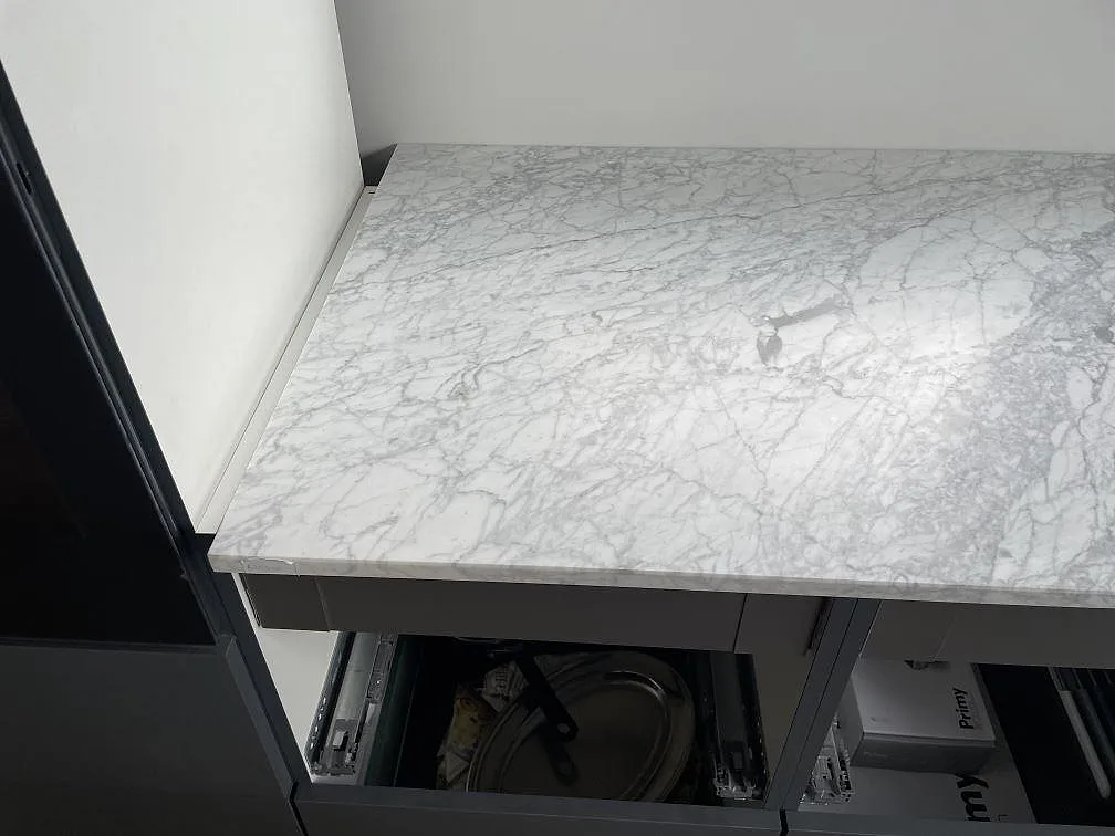 Detalj av installerad bänkskiva i matt Carrara C marmor över mörka köksstommar i Mölndal.