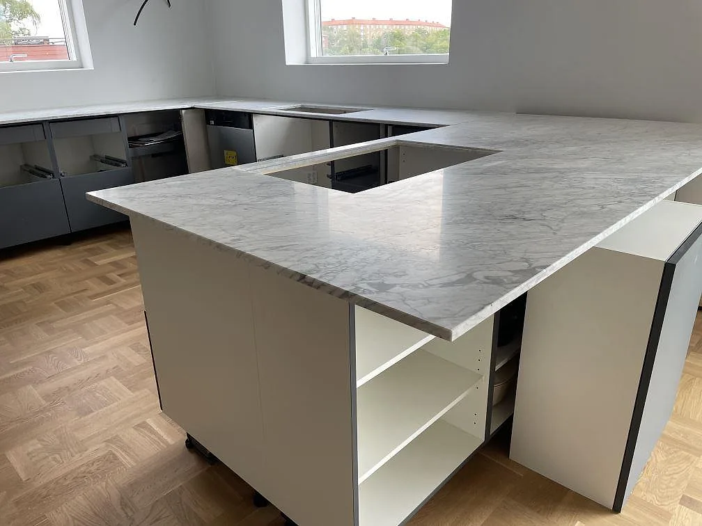 Köksbänkskiva i matt Carrara C marmor med köksö och U-format kök vid stora fönster i Mölndal.