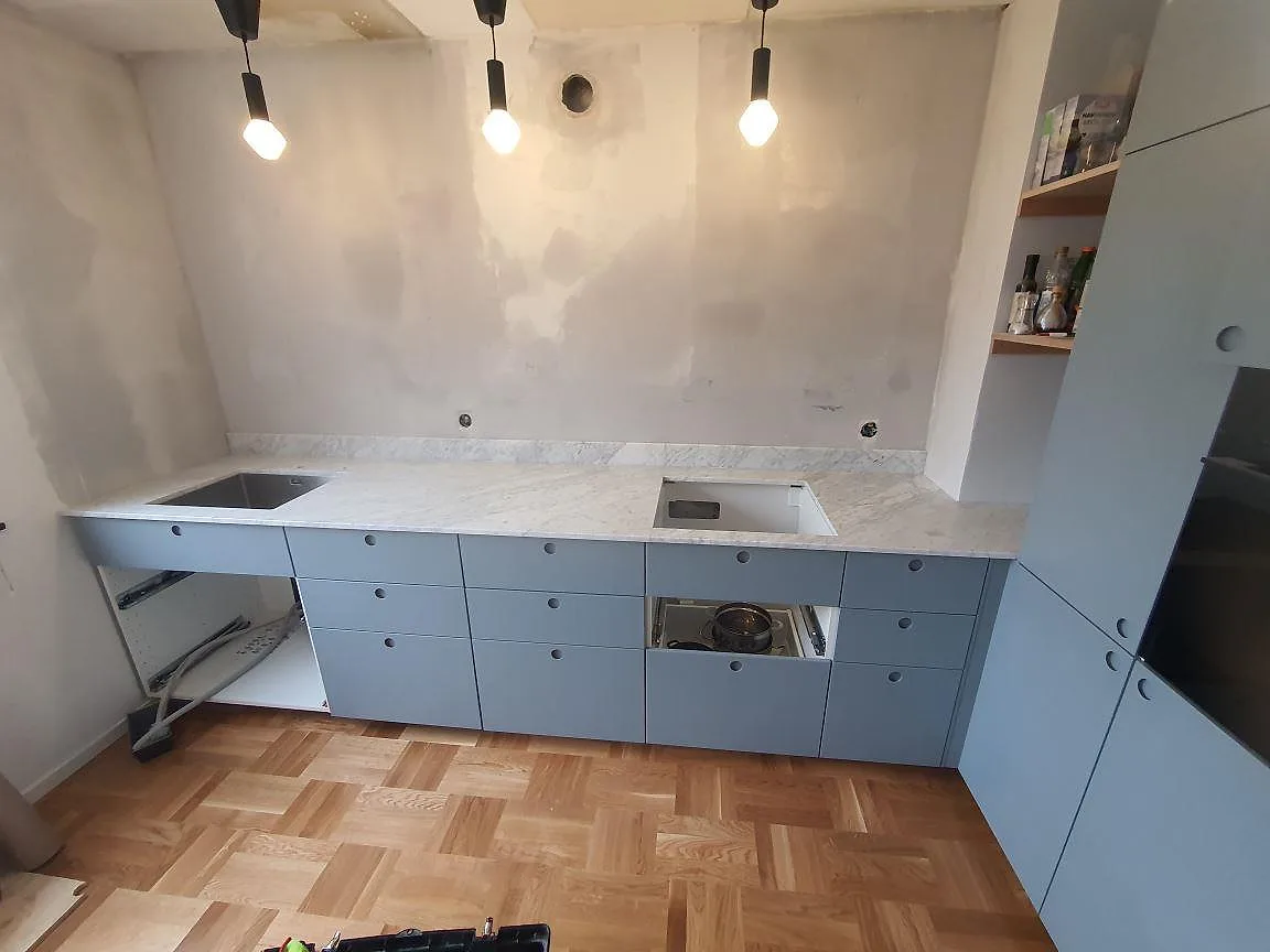 Köksbänkskiva i Carrara C marmor, matt, med diskho, hällöppning och låg stänkkant i ett kök i nacka.