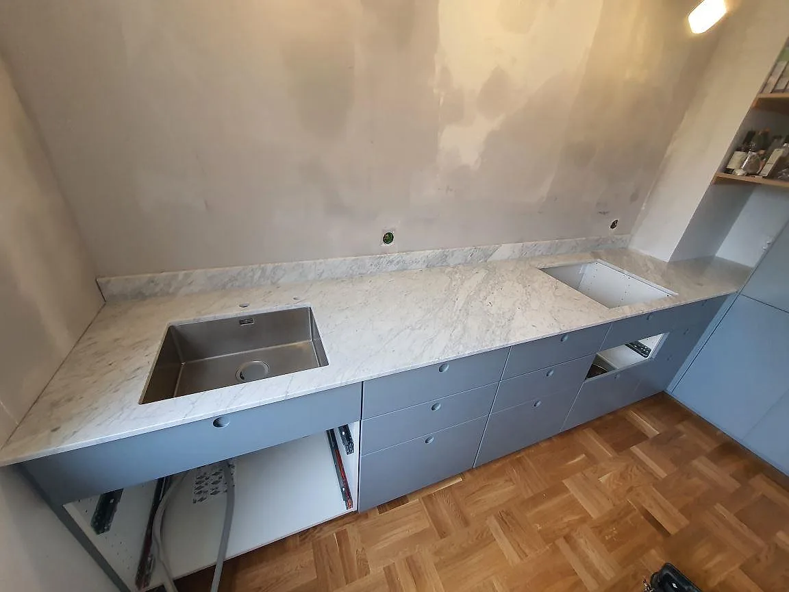 Köksbänkskiva i vit Carrara C marmor, matt yta, med underlimmad rostfri diskho och uppvikt stänkkant i ett kök i Nacka.