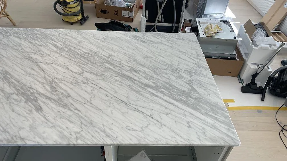 Vy ovanifrån över köksö i matt Carrara C marmor med tät grå ådring i ett ljust kök i Nättraby.