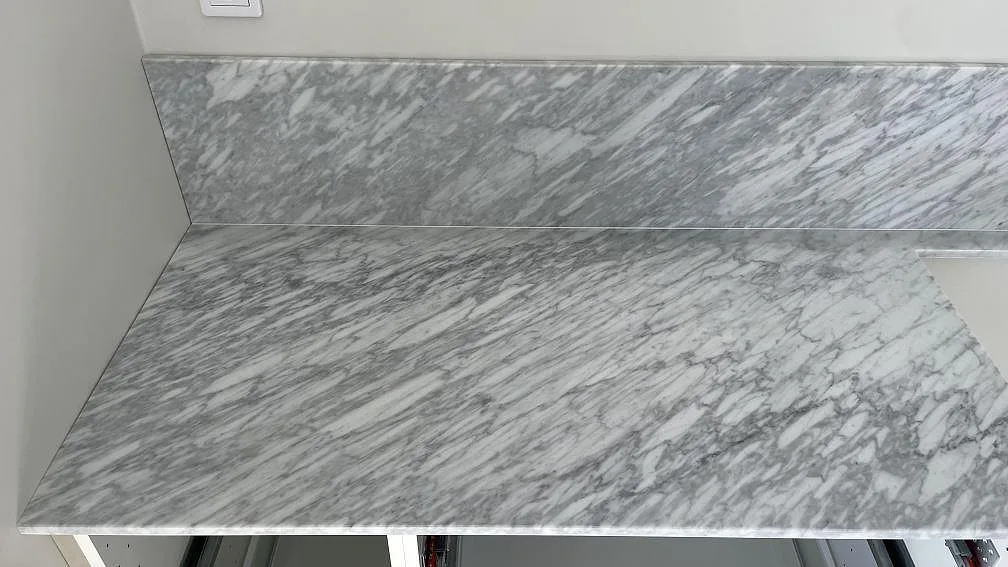 Närbild på väggbänk i matt Carrara C marmor med sammanpassad låg stänkkant och kraftig grå ådring i Nättraby.