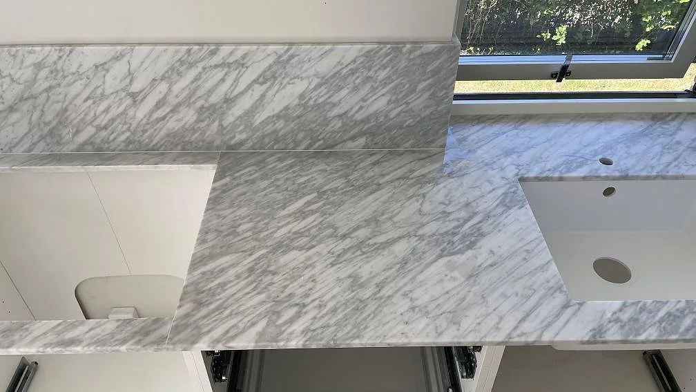 Detalj av matt Carrara C bänkskiva med hoöppning, kranhål och stänkkant framför fönstret i Nättraby.