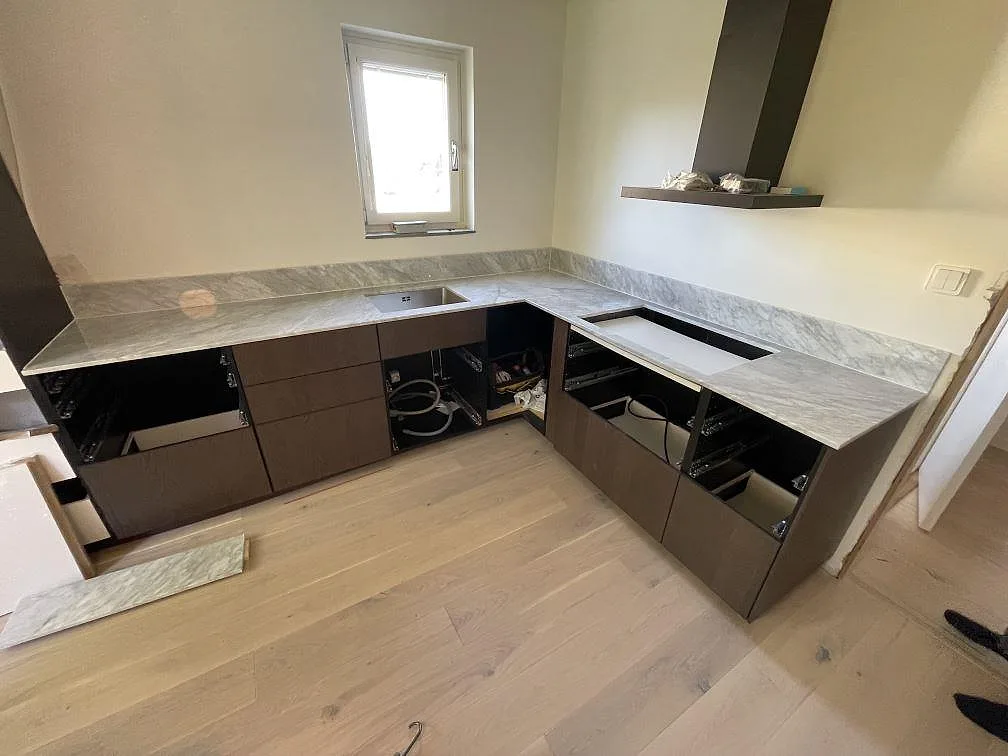 L-formad köksbänkskiva i polerad Carrara C-marmor med låg stänkkant och förberedd öppning i ett kök i Norrtälje.
