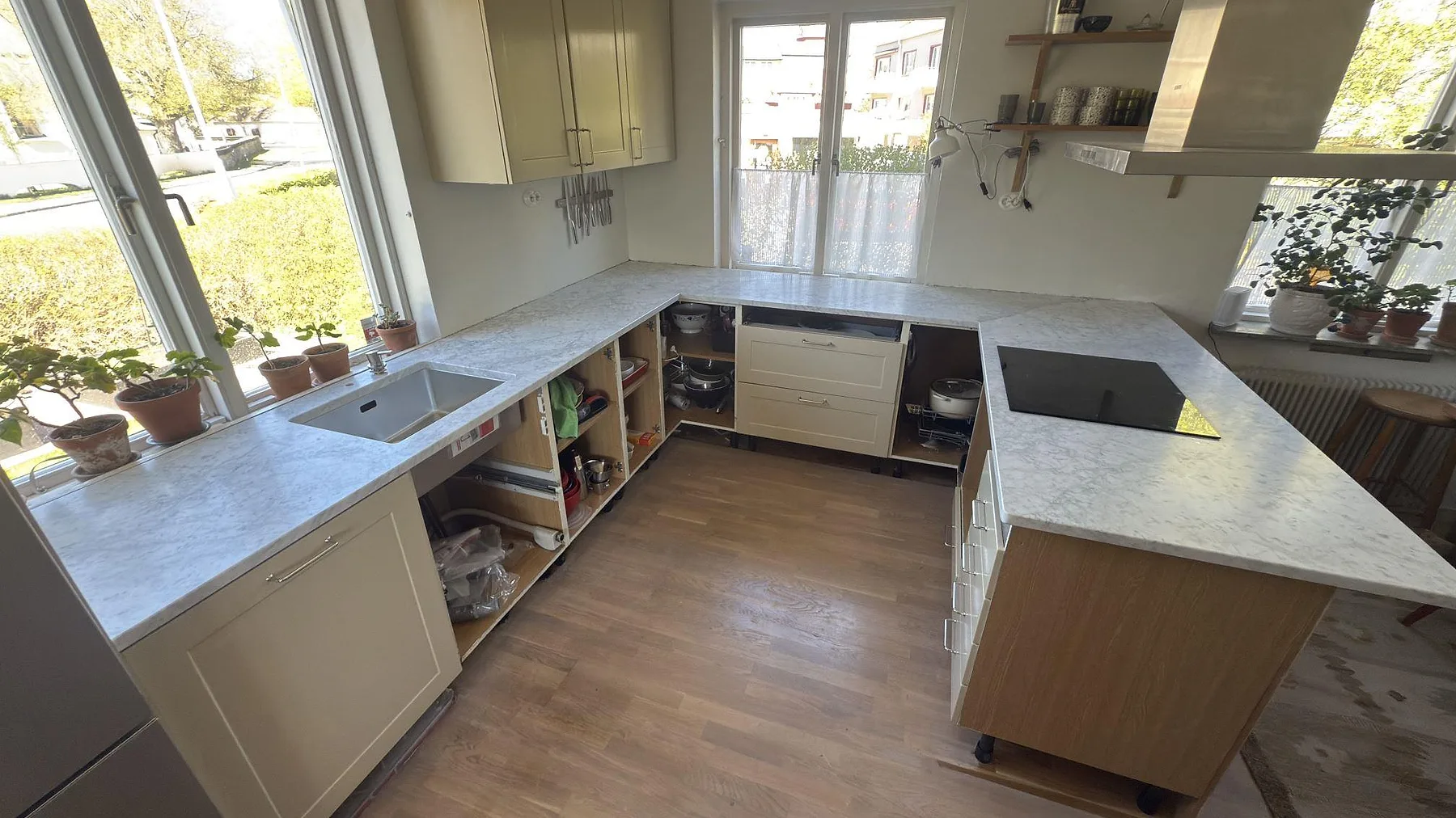 Köksbänkskiva i Carrara C, matt vit marmor med grå ådring, i ett L-format kök med fristående köksö, underlimmad diskho och infälld induktionshäll i Nyköping.