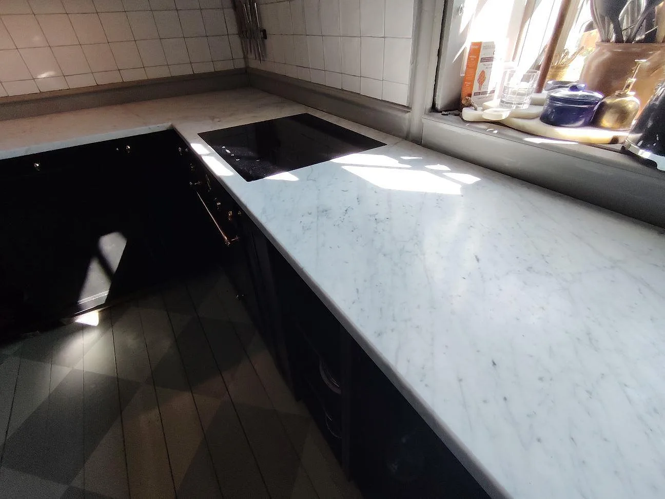 Rak köksbänkskiva i matt Carrara C marmor med infälld svart häll och synlig grå ådring vid fönster i Örsundsbro.