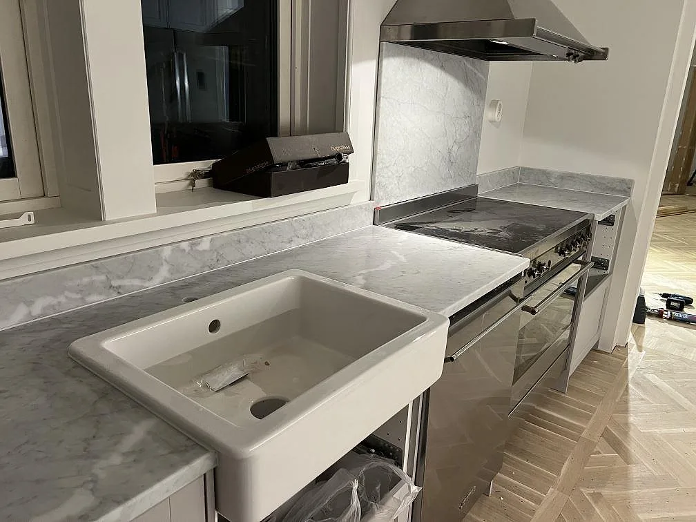 Närbild av matt Carrara C marmor som köksbänkskiva runt ho och spis med uppvikt stänkkant i Österskär.