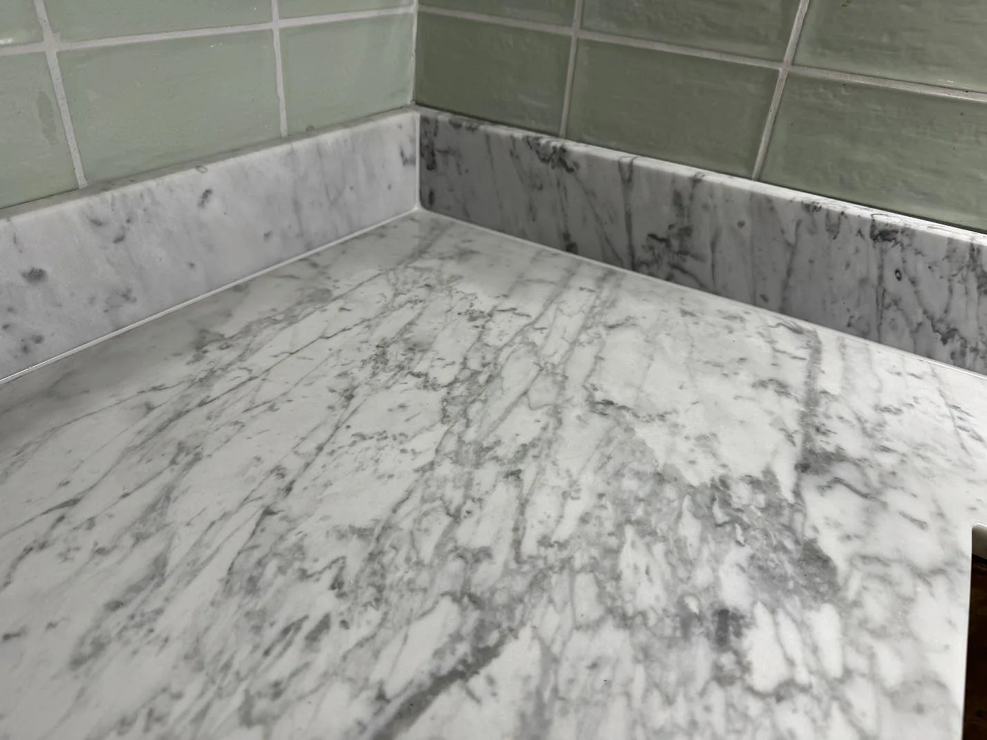 Ådrad Carrara C marmor i matt köksbänkskiva, fotograferad nära den uppvikta stänkanten i ett kök i Rockneby.