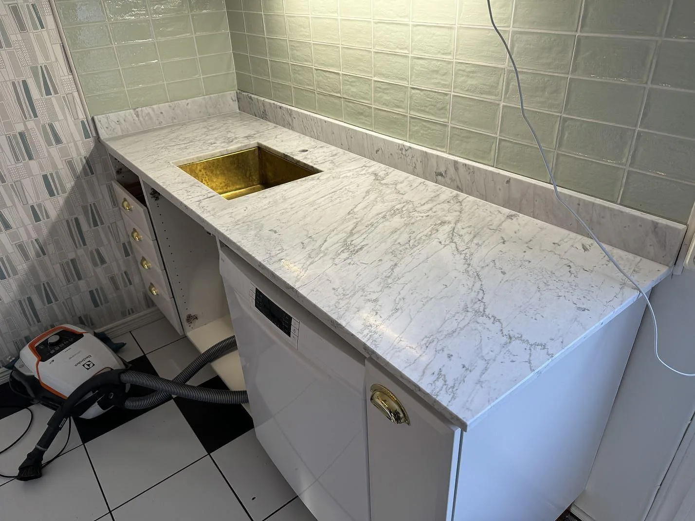 Köksbänkskiva i Carrara C marmor med mässingsfärgad diskho, vit skåpinredning och installationsverktyg i Rockneby.