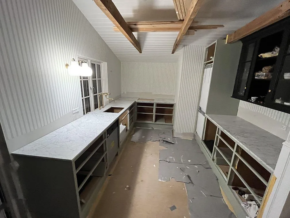 Köksbänkskiva i Carrara C marmor, matt, i ett vinklat U-format kök under montering i Rørvig, med underlimmad diskho och mässingsblandare.