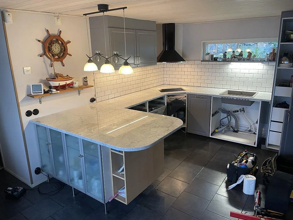 Polerad köksbänkskiva i Carrara C marmor, 30 mm, med rundad peninsula och hällöppning i ett kök i Ronneby.