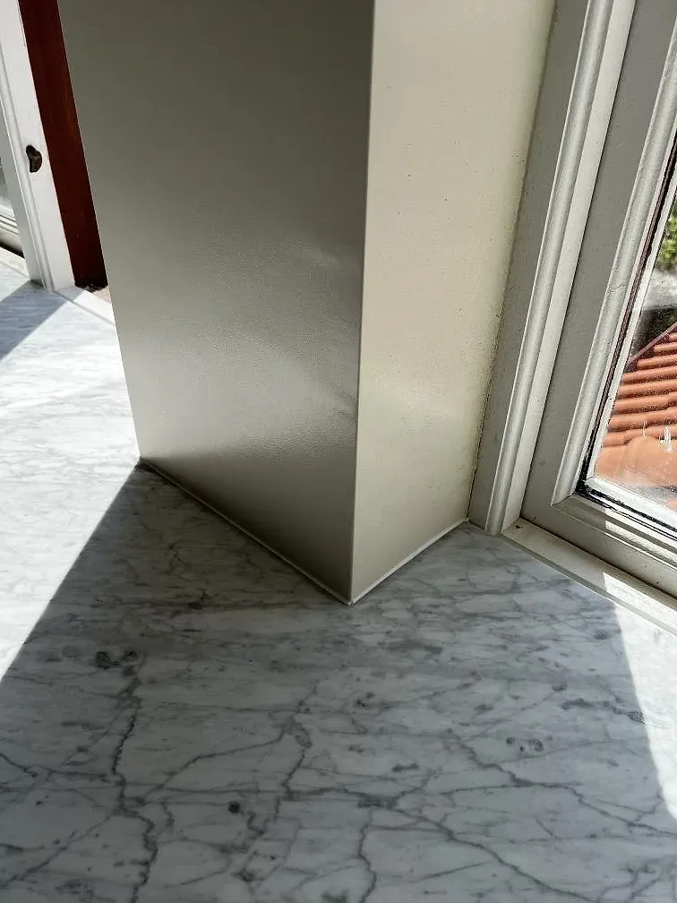 Hörn och väggbeklädnad i matt Carrara C marmor vid fönster i ett badrum i Rydsgård.
