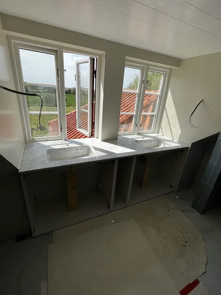 Badrum under montering med Carrara C marmor som bänkskiva och väggbeklädnad framför höga fönster i Rydsgård.