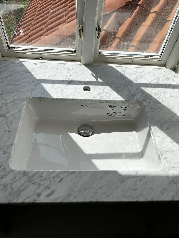 Närbild på matt Carrara C marmor som badrumsbänkskiva med vitt tvättställ och grå ådring i Rydsgård.