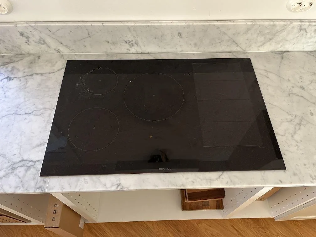 Detalj av svart induktionshäll i en matt Carrara C marmorbänkskiva i köket i Saltsjö Duvnäs, med grå ådring runt hällen.