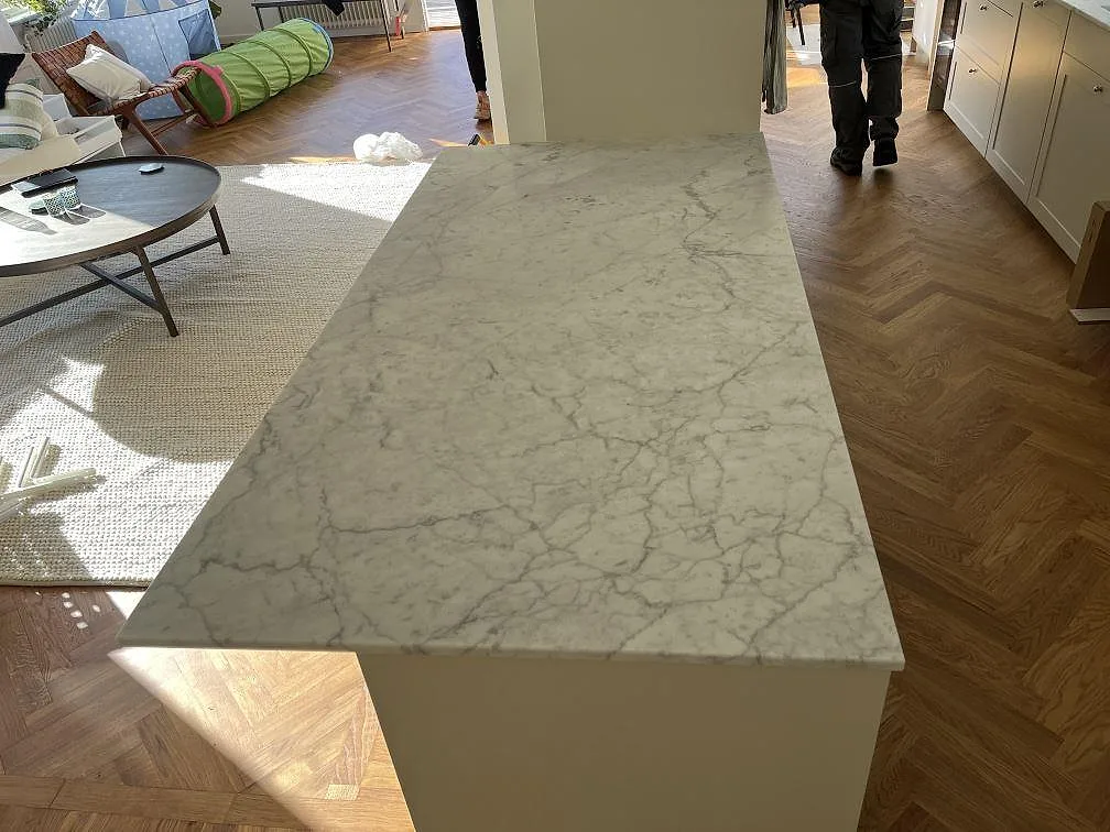 Fristående arbetsyta i matt Carrara C marmor i Saltsjö Duvnäs, fotograferad mot fiskbensgolv och det L-formade köket.