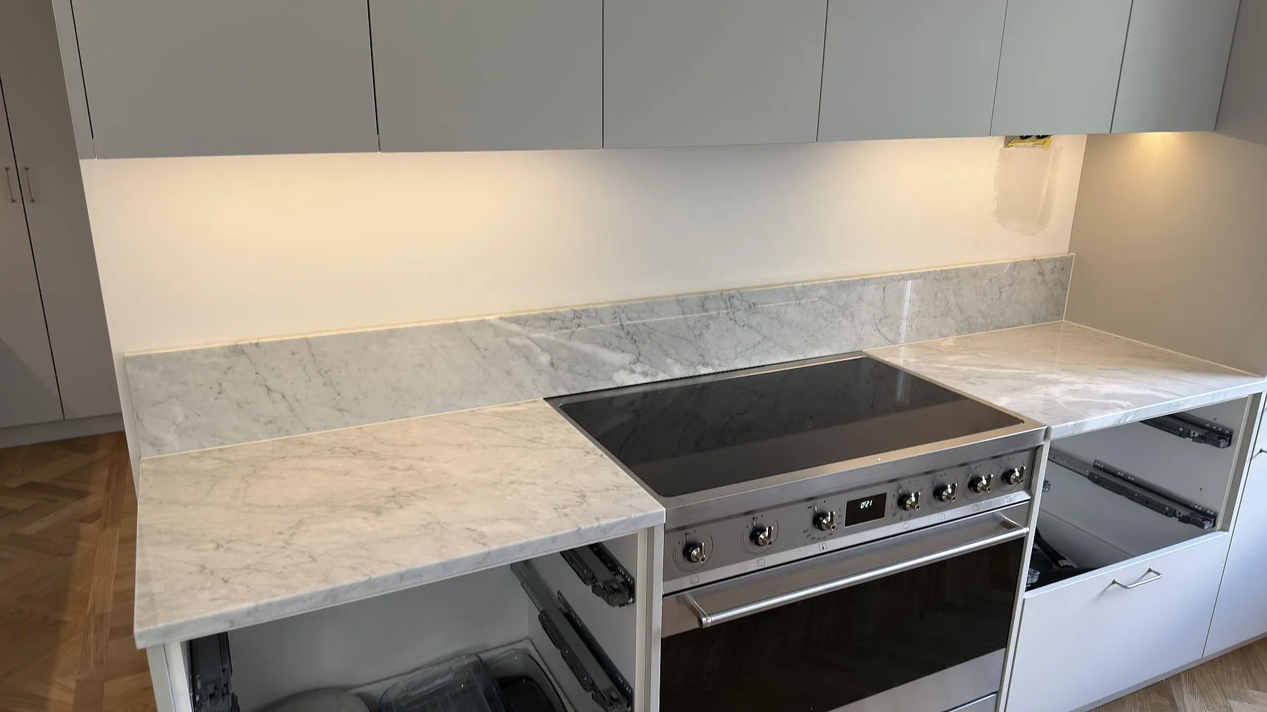 Polerad Carrara C marmor runt spispartiet med låg stänkkant under överskåp i ett kök i Saltsjöbaden.