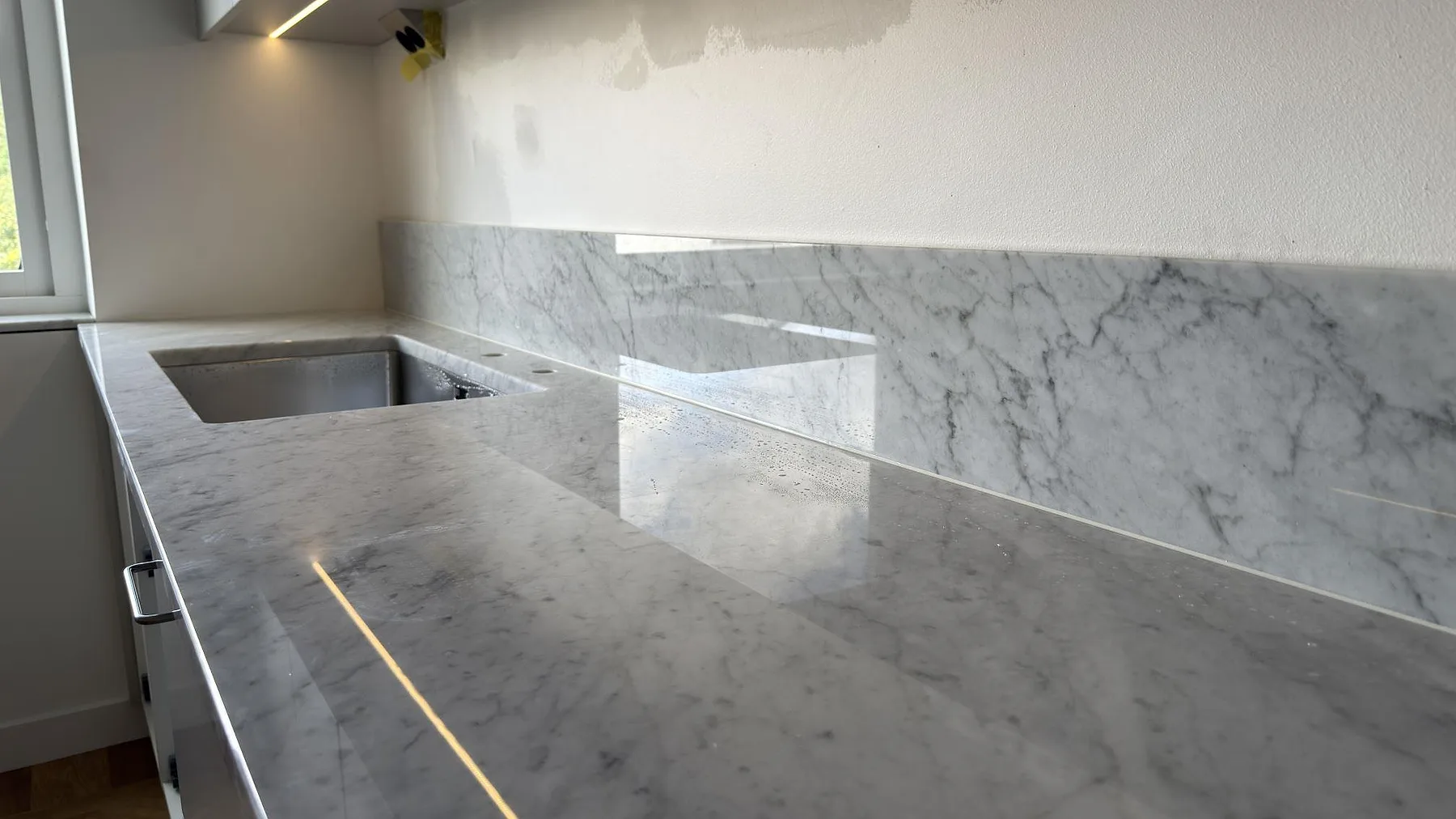 Närbild på polerad Carrara C marmor vid diskhoöppningen, med grå ådring och låg stänkkant i köket i Saltsjöbaden.