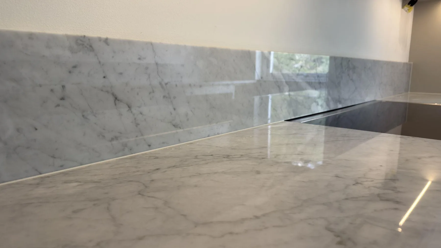 Detaljbild av polerad Carrara C marmor med blank ådrad yta och låg stänkkant bredvid spispartiet i Saltsjöbaden.