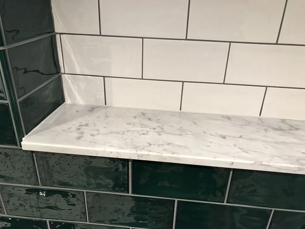 Bänkskiva i vit Carrara C-marmor, matt, monterad i hörn mot vit och grön kakel i ett kök i Skanör.