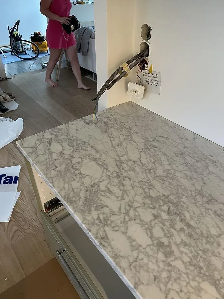 Närbild av köksö i matt Carrara C marmor med vattenfallsida, öppna stommar och monteringsutrustning i Skanör.