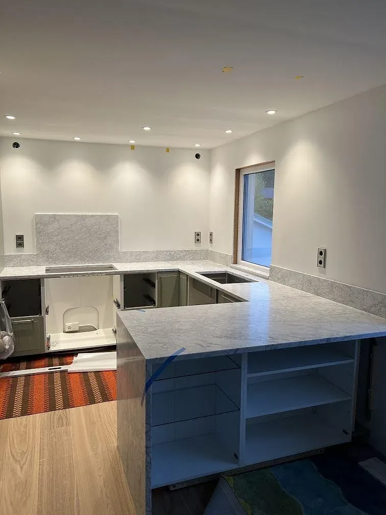 Kök i Skanör under montering med bänkskivor och köksö i matt Carrara C marmor samt grå stommar.