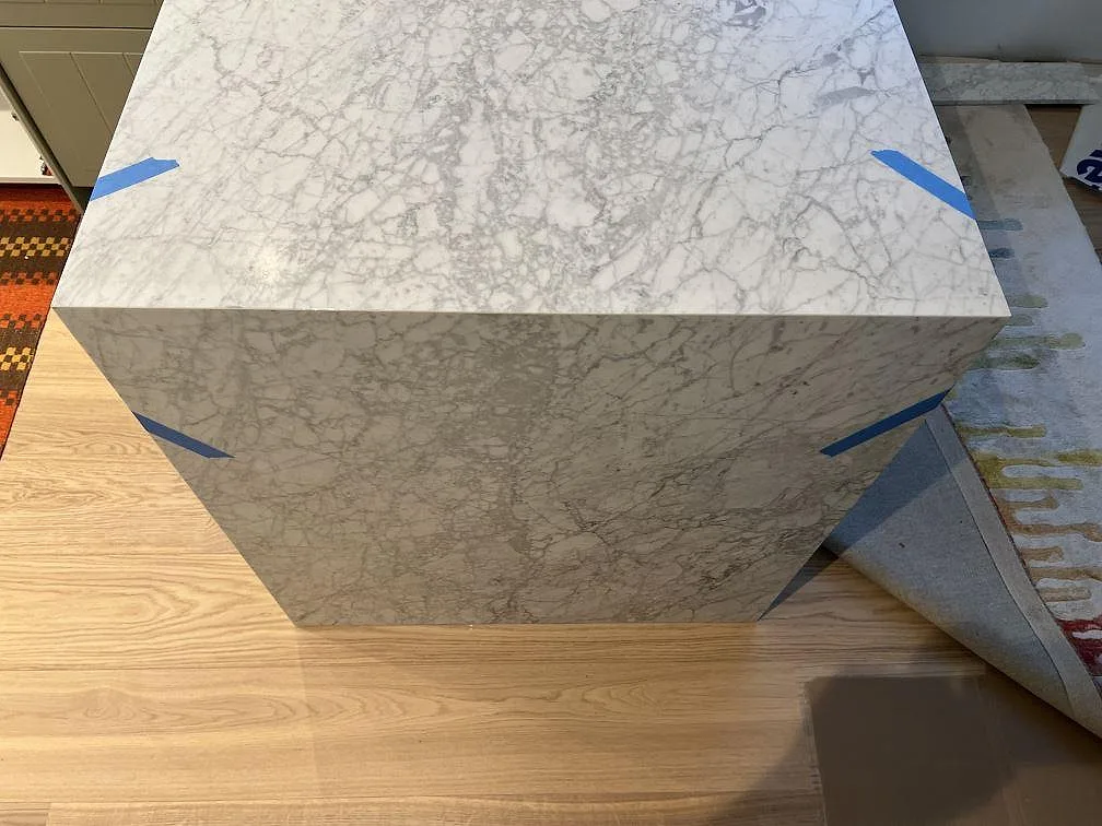 Köksö i matt Carrara C marmor med vattenfallsida och synlig grå ådring under montering i Skanör.