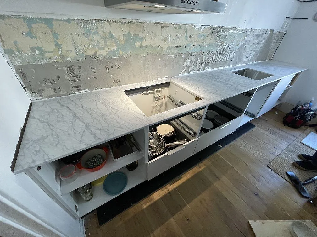 Matt köksbänkskiva i Carrara C marmor med diskhozon och hällöppning i ett kök under montering i Skarpnäck.