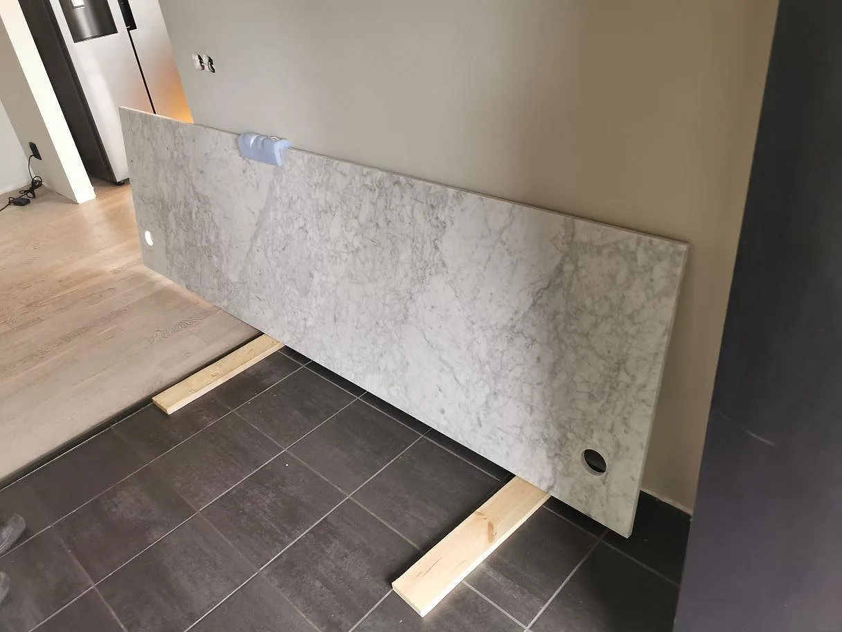 Måttkapad bänkskiva i vit Carraramarmor Carrara C med hål för blandare, lutad mot väggen inför montering i Skillingaryd.