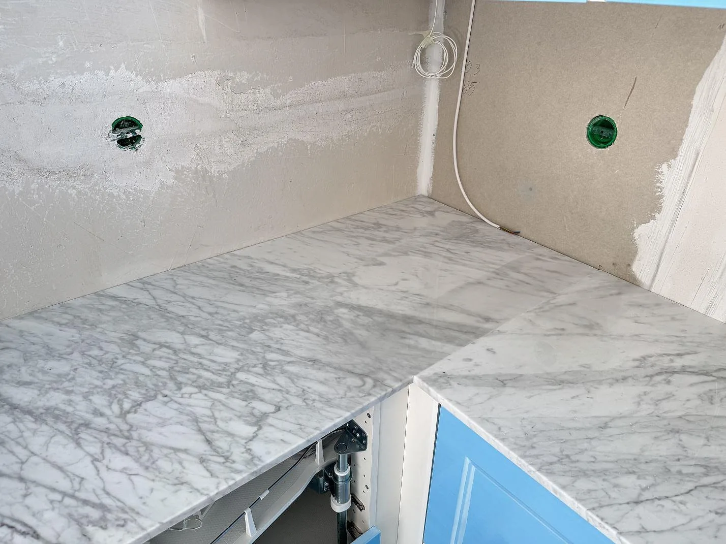 Köksbänkskivor i polerad Carrara C-marmor, lagda i vinkel på blå köksstommar under montering i Skillinge.