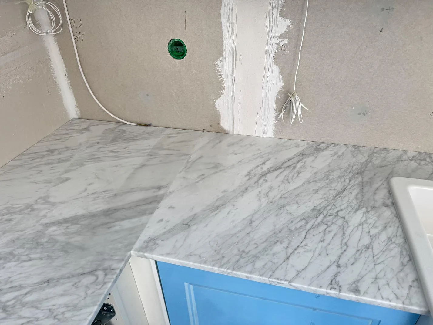 Vinklad köksbänkskiva i polerad Carrara C-marmor med tät grå ådring och synlig diskho i Skillinge.