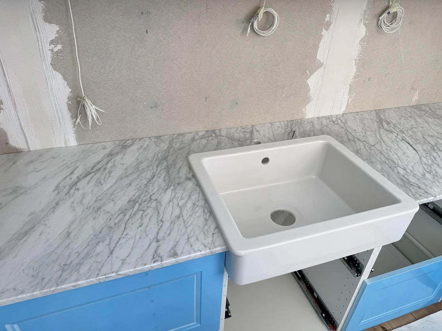 Polerad Carrara C-marmorbänkskiva med vit diskho och blå köksfronter i ett kök under montering i Skillinge.