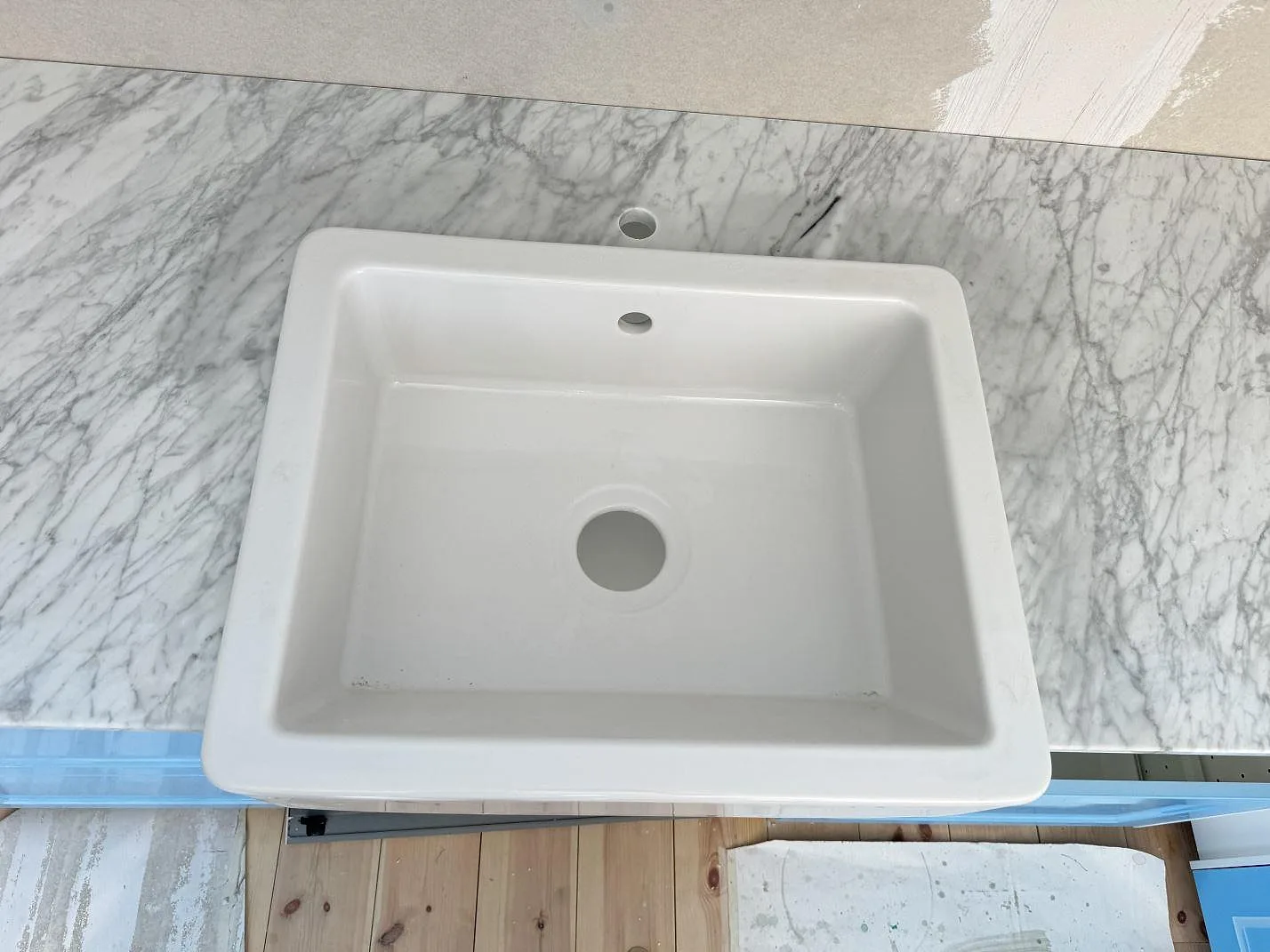Topvy av vit diskho och polerad Carrara C-marmorbänkskiva med grå ådring i ett kök i Skillinge.