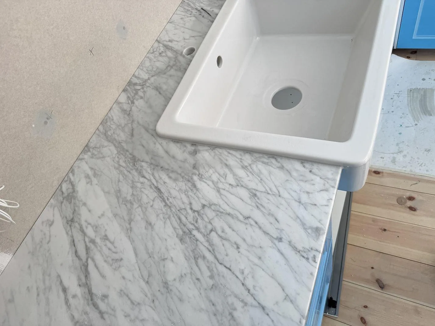 Detalj av polerad Carrara C-marmorbänkskiva vid vit diskho och trägolv i kök i Skillinge.
