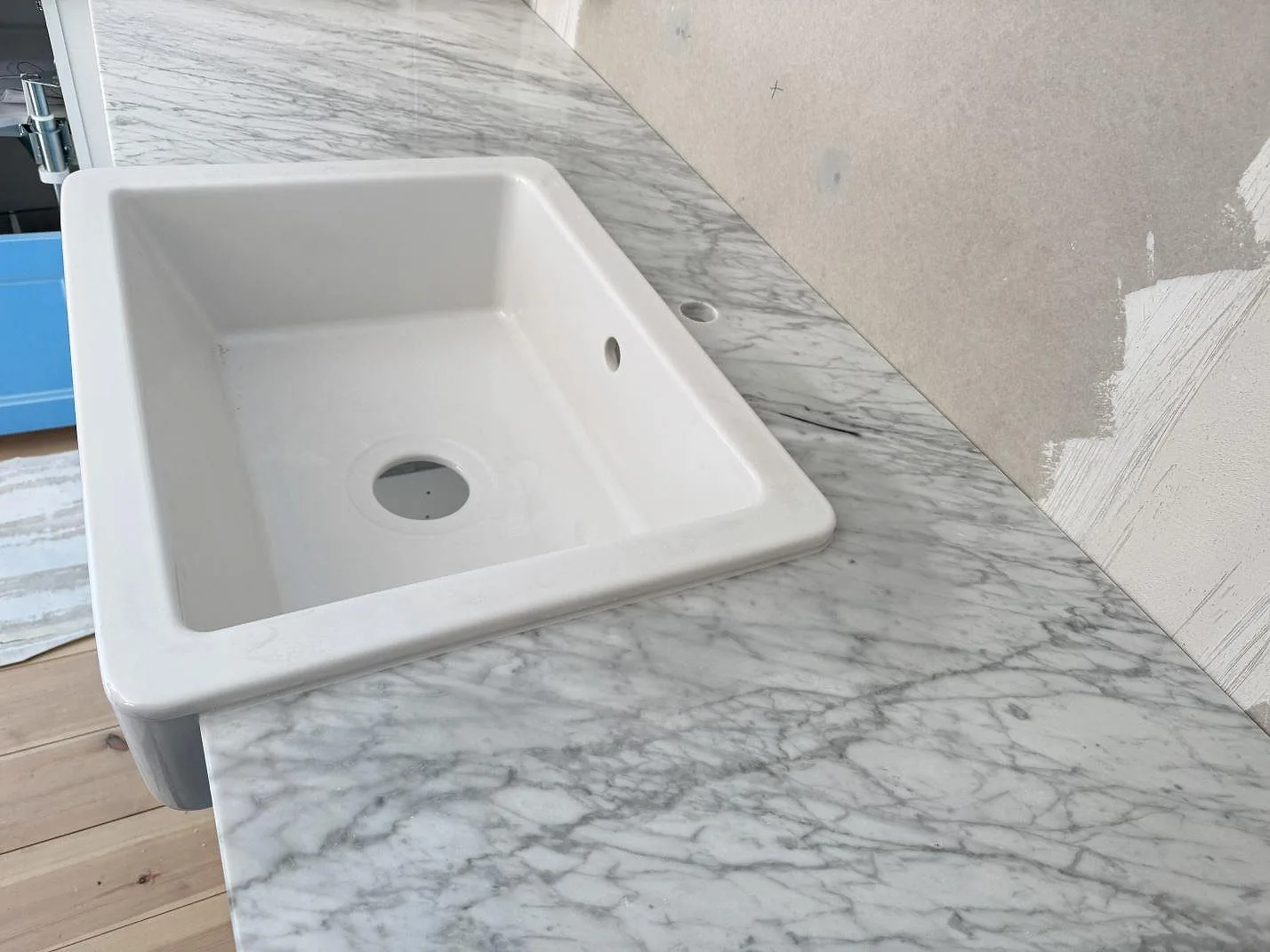 Köksbänkskiva i polerad Carrara C-marmor runt en vit diskho, fotograferad snett ovanifrån i Skillinge.
