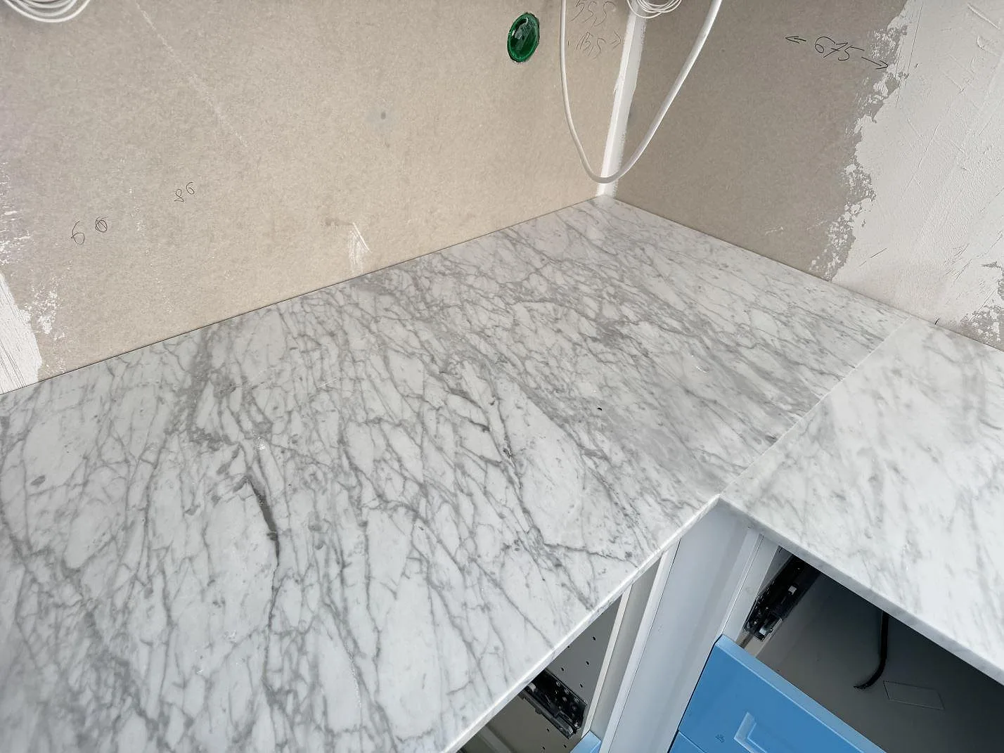 Hörnparti av köksbänkskiva i polerad Carrara C-marmor med grå ådring på blå stommar i Skillinge.