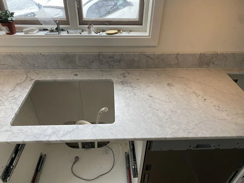 Matt köksbänkskiva i Carrara C marmor med underlimmad rostfri diskho, låg stänkkant och fönster i Skummeslövsstrand.