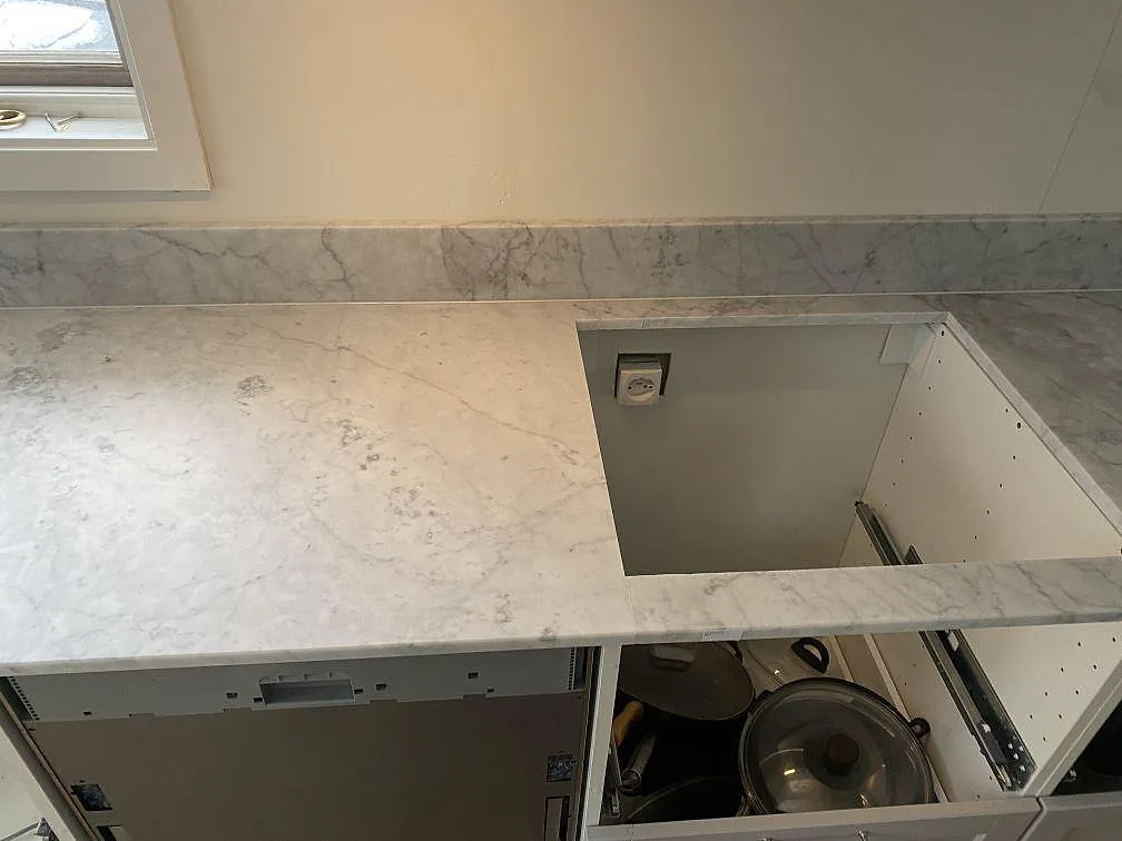 Carrara C marmorbänkskiva i matt finish med hällurtag och uppvikt stänkkant i ett vitt kök i Skummeslövsstrand.