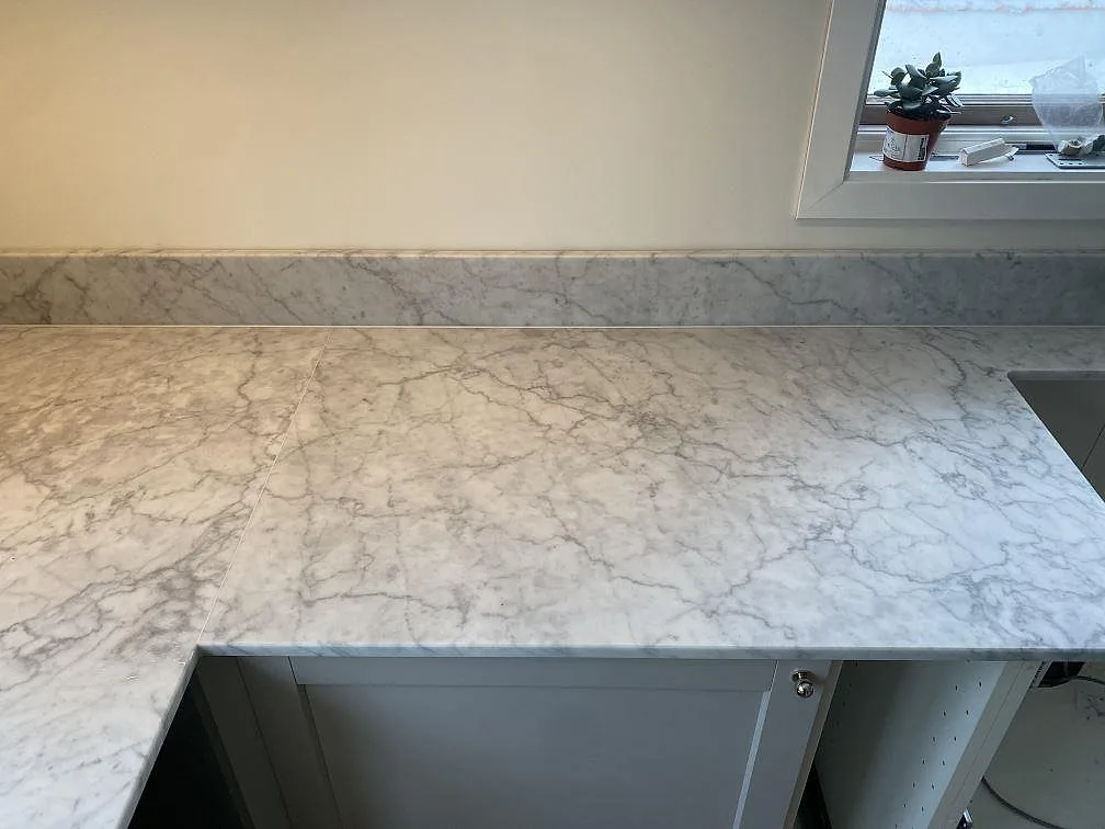 Närbild på matt Carrara C marmor med låg stänkkant, synlig ådring och diskhozonen vid fönstret i Skummeslövsstrand.