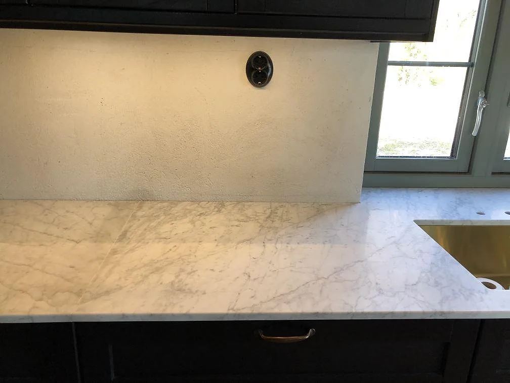 Lång bänkskiva i vit Carrara C-marmor med grå ådring och underlimmad diskho i ett kök i Skurup.