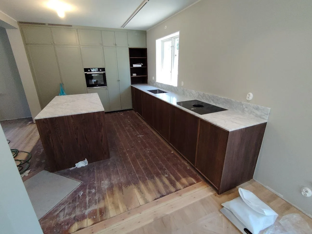 Köksbänkskiva i matt Carrara C-marmor med uppvikt stänkkant och halvö på valnötstonade underskåp i Sollentuna.
