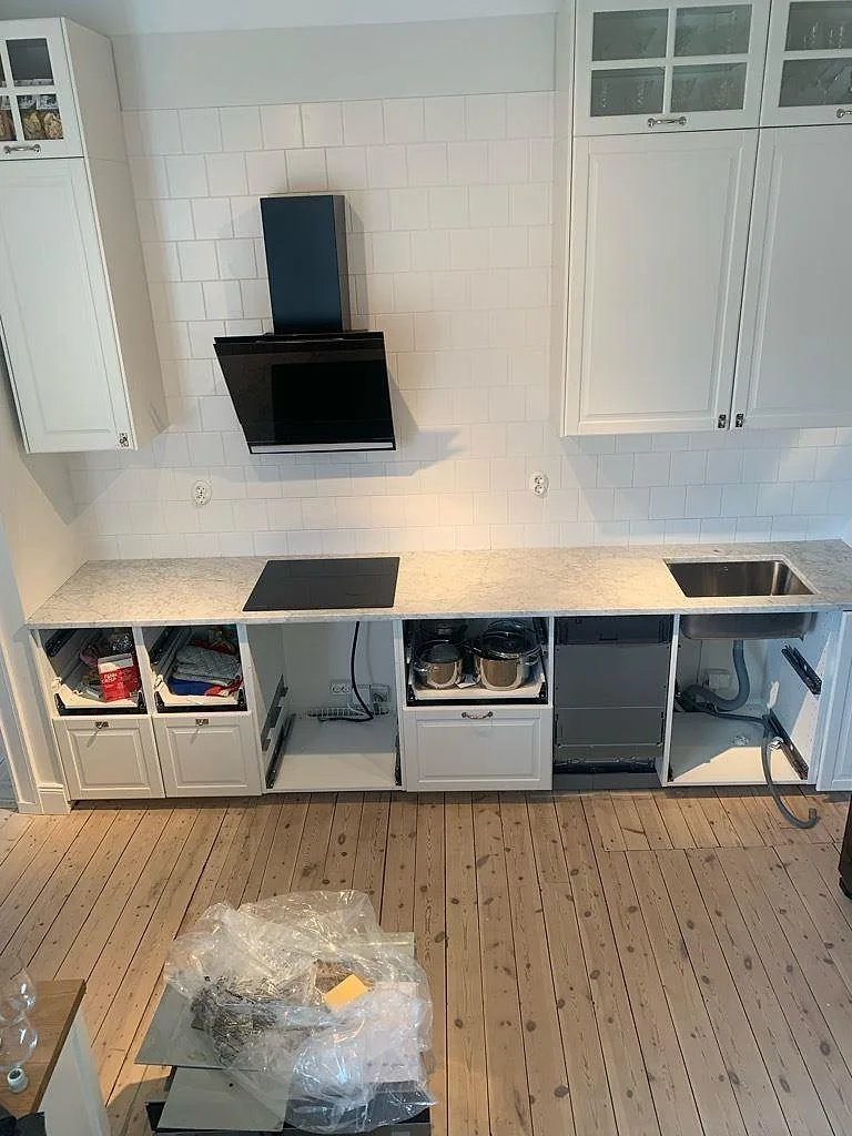 Köksbänkskiva i polerad Carrara C marmor, 30 mm, med svart häll, svart fläktkåpa och vit kakelvägg i Solna.